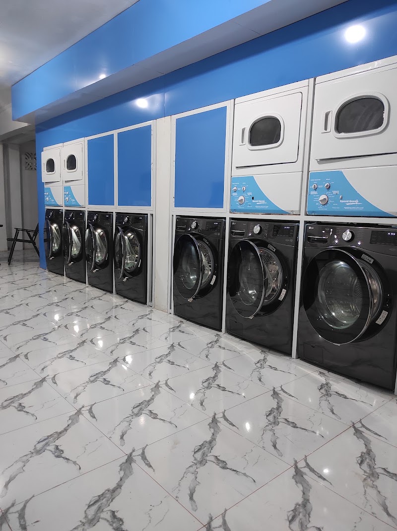 A clean laundromat interior with a polished marble-patterned tile floor and a row of stacked commercial dryers above front-load washing machines along a blue wall.