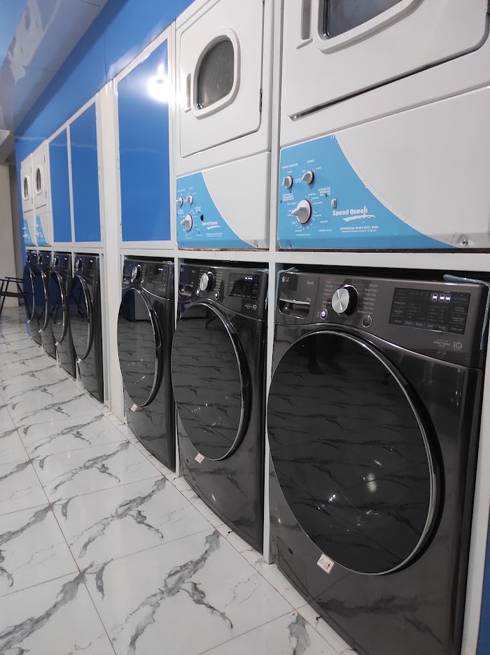 A close perspective shot focusing on commercial Speed Queen dryers mounted directly over black LG front-load washing machines.
